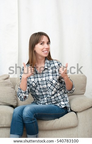 Smiling attractive young woman sitting on couch in her living room. Portrait of beautiful brunette girl in casual shirt gesturing and smiling