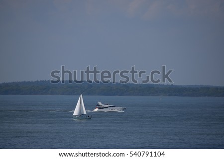 White sail boat and a speed boat on the open sea with the horizon