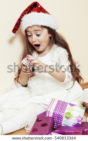 little cute girl in santas red hat waiting for Christmas gifts. smiling adorable kid. White new dress home interior 