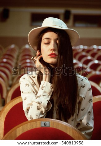 portrait of a pretty girl hipster in a movie theater wearing hat, dreaming alone