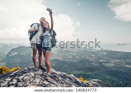 Two hikers taking selfie from top of the mountain with valley view on the background