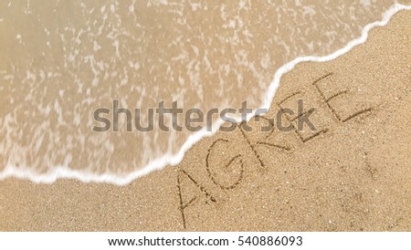 Handwriting words "AGREE" on sand of beach