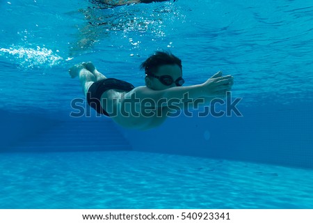 Happy young asian kid with swim goggles underwater - breast stroke in middle of swimming pool, smile relax face swimmer have fun activity