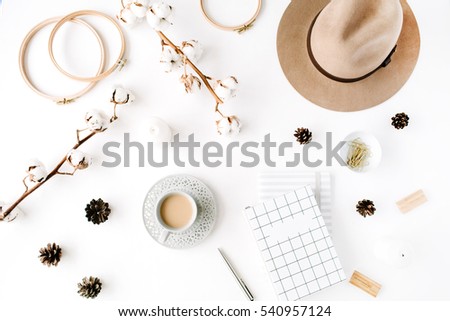 Flat lay trendy creative feminine accessories arrangement with coffee, cotton branch and diary. Hat, cotton branch, notebook, coffee cup, fir cone, golden clips on white background. Top view