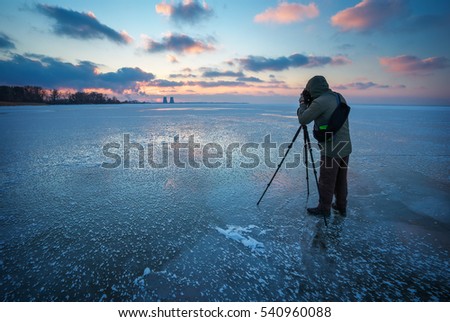 Photographer takes a picture of sunset on a frozen river in winter

