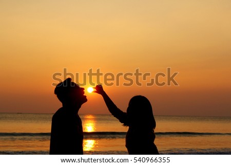 Silhouette of women and men holding the sun at sunset on the beach