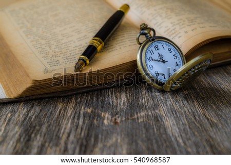 Open vintage book and clock on the old wooden background.