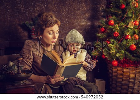 Mother reads to his son the book near a Christmas tree. Christmas card.