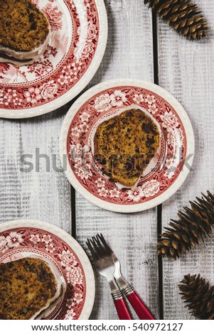 Spicy Pumpkin Cake with nuts and cranberries drizzled icing cut into pieces in bright painted plates on the wooden background with fir cones. Selective focus. Toned image 