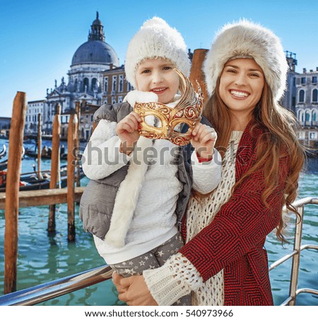 Another world vacation. Portrait of happy modern mother and child travellers on embankment in Venice, Italy while holding Venetian mask