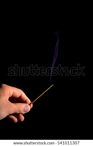 hand with burning incense stick and violet smoke trail