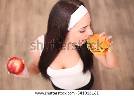 Young beautiful asian girl making choice between hamburger and a red apple, healthy eating and lifestyle concept.