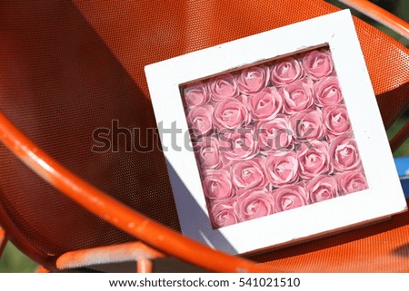 Many beautiful pink roses in white picture frame on orange chair