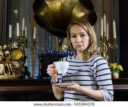 portrait of a young woman stends near the fireplace, happy smiling girl drinks tea