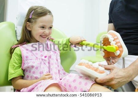 Smiling little girl in dentists chair, being educated about proper tooth-brushing by her paediatric dentist. Early prevention, raising awareness, oral hygiene demonstration concept.  Royalty-Free Stock Photo #541086913
