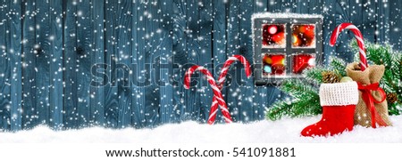 Santa boot and bag with candy cane, gifts and cones on wooden wall background and glowing lights outside the window