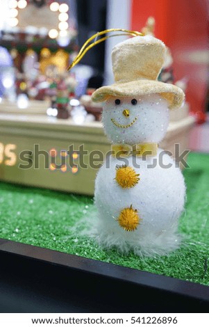  snowman wool doll on snow set up with xmas tree, red&blue gift box, sled, bokeh decorations light ball christmas background