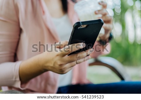 Asian Woman typing text message on smart phone in a cafe. Cropped image of young woman sitting at a chair with a coffee using mobile phone. Royalty-Free Stock Photo #541239523