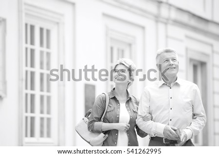 Happy middle-aged couple standing with arm in arm outside building