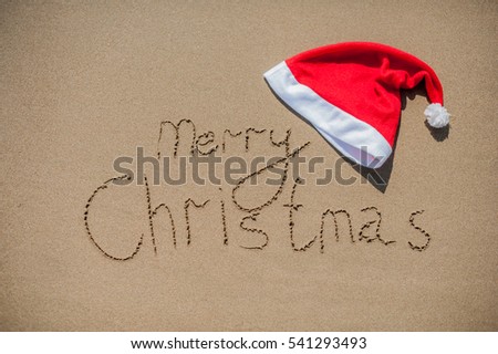 inscription on the wet sand and cap of Santa Claus Christmas in tropical climate concept