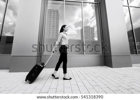 Full length side view of young businesswoman walking with luggage on sidewalk against building