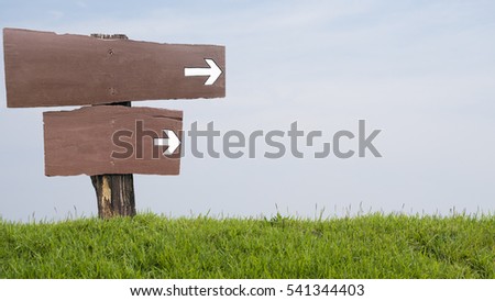 Wooden sign with an arrow pointing the way. Embroidered on the grassy knoll Background sky