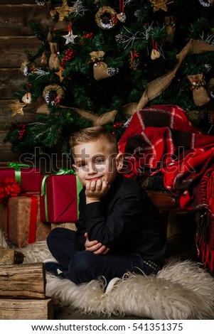 Very nice boy sits near a Christmas tree smiling happily wrapped in a red blanket
