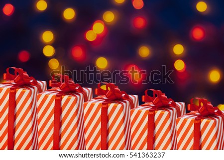 Christmas Gifts with red ribbon on a dark blue background with red yellow bokeh. Sale. Happy New Years Decorations.