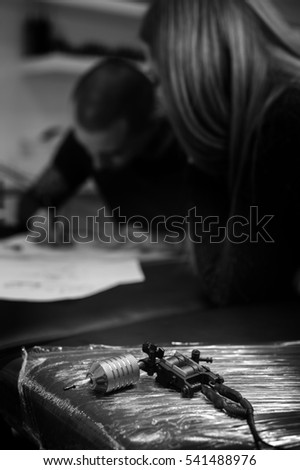 Professional tattoo machine, closeup. Male tattooer and female client creating sketch. Shallow depth of field, black and white image