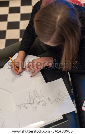Young attractive blonde woman sitting in tattoo parlor and creating sketch for tattooing