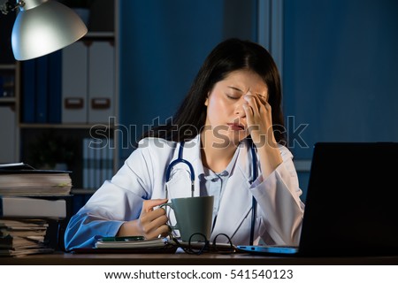 Closeup portrait sad unhappy health care professional with headache stressed sleepy holding cup of coffee. Nurse doctor with migraine overworked overstressed. pretty mixed race asian chinese woman