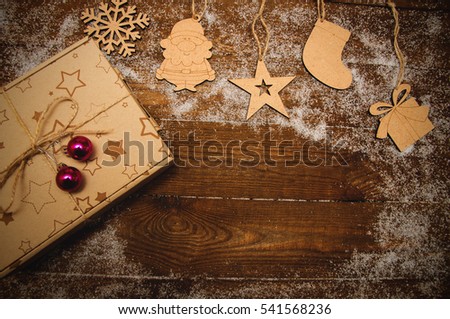 Christmas gift box with natural wooden figures snowman, santa claus, mitten, starhanging on a wooden boards background and snowflake 