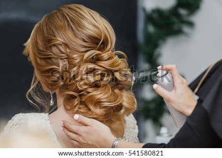 Master stylist makes the bride wedding hairstyle using spray lacquer fixing Royalty-Free Stock Photo #541580821