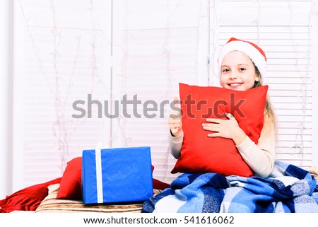 cute blonde smiling girl with blue checkered plaid hugs red pillows on white studio background, copy space