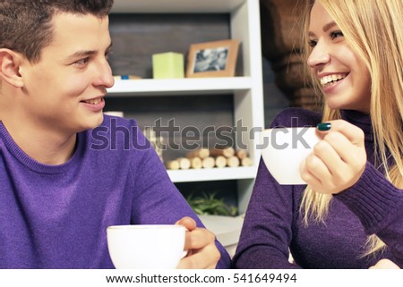 Loving young couple sitting in the cafeteria, talking and smiling. Drink hot coffee.