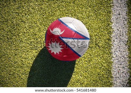 football ball with the national flag of nepal lies on the green field near the white line