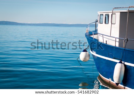 
A blue fishing boat in the sea and in the background mountains surrounding the sea