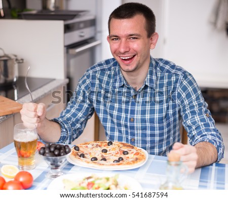 young man eating pizza and salad in the kitchen at home