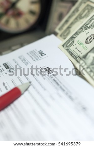 Tax Season: 1040 U.S. Individual Income Tax Return Form vertical top side view office laptop bank notes vintage clock background and a white red pen prepare for taxation foreground - image