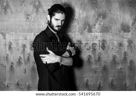 sad young bearded gothic hipster man standing against a background of a wooden wall. a man dressed in black