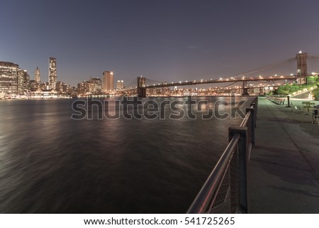 Night view of Manhattan, New York. Reflections of lights and skyscrappers in water. Calm colors, deep blue sky.