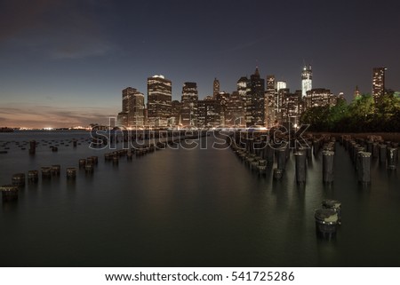 Night view of Manhattan, New York. Reflections of lights and skyscrappers in water. Calm colors, deep blue sky.
