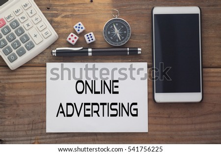 Online Advertising written on paper,Wooden background desk with calculator,dice,compass,smart phone and pen.Top view conceptual.