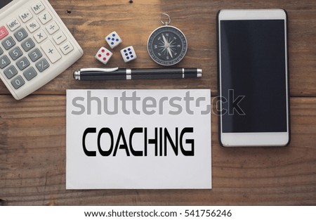 Coaching  written on paper,Wooden background desk with calculator,dice,compass,smart phone and pen.Top view conceptual.