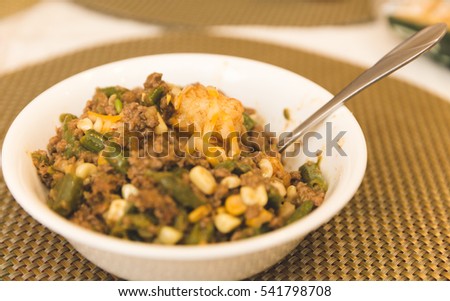 Casserole in a white bowl with hamburger, green beans, tater tots, and corn.