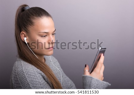Portrait of a young woman using smartphone with headphones on gray background.