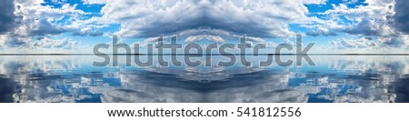 Spectacular blue and white panoramic Cumulus cloudscape with clear water reflections. Photograph was shot at sea from the deck of a boat looking toward land.