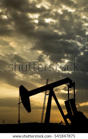 silhouette of crude oil pump in the oil field on a cloudy sunrise  
