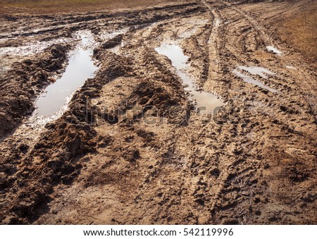 Backdrop of thick viscous slippery tracks from tires on clay off-road in provincial village sunny spring evening after rain with place for text on gray surface