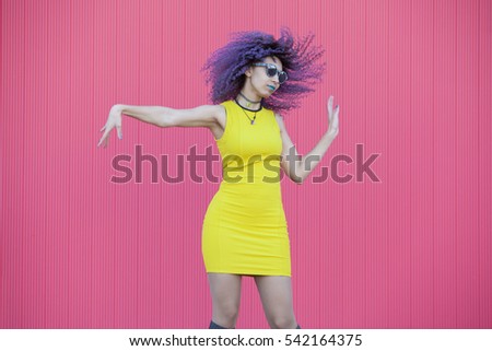 teen woman with colored purple afro hair dancing on a pink wall